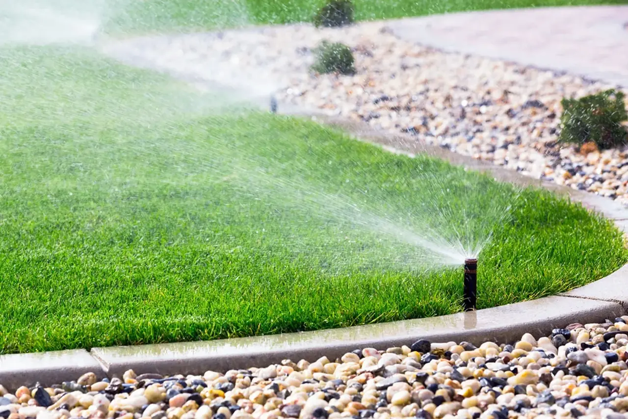 Sprinklers watering a lawn along a landscaped border